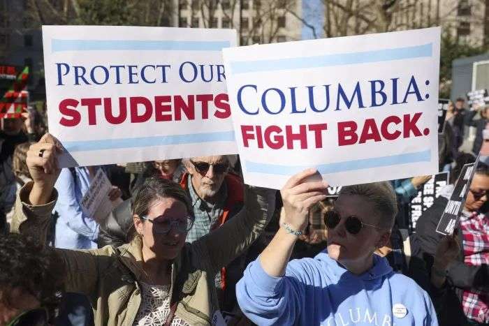Protestors at a rally for higher education hold signs that read 