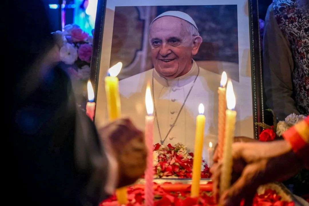 People light candles as they pay respects in front of a portrait of Pope Francis during a condolence meeting in New Delhi, following the news of his death.