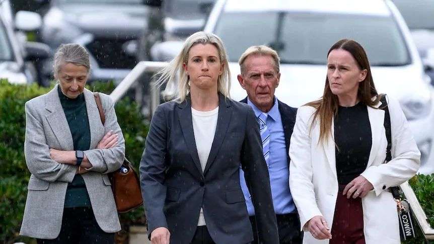 A young woman wearing a grey suit with a white undershirt stands outside court with sunglasses