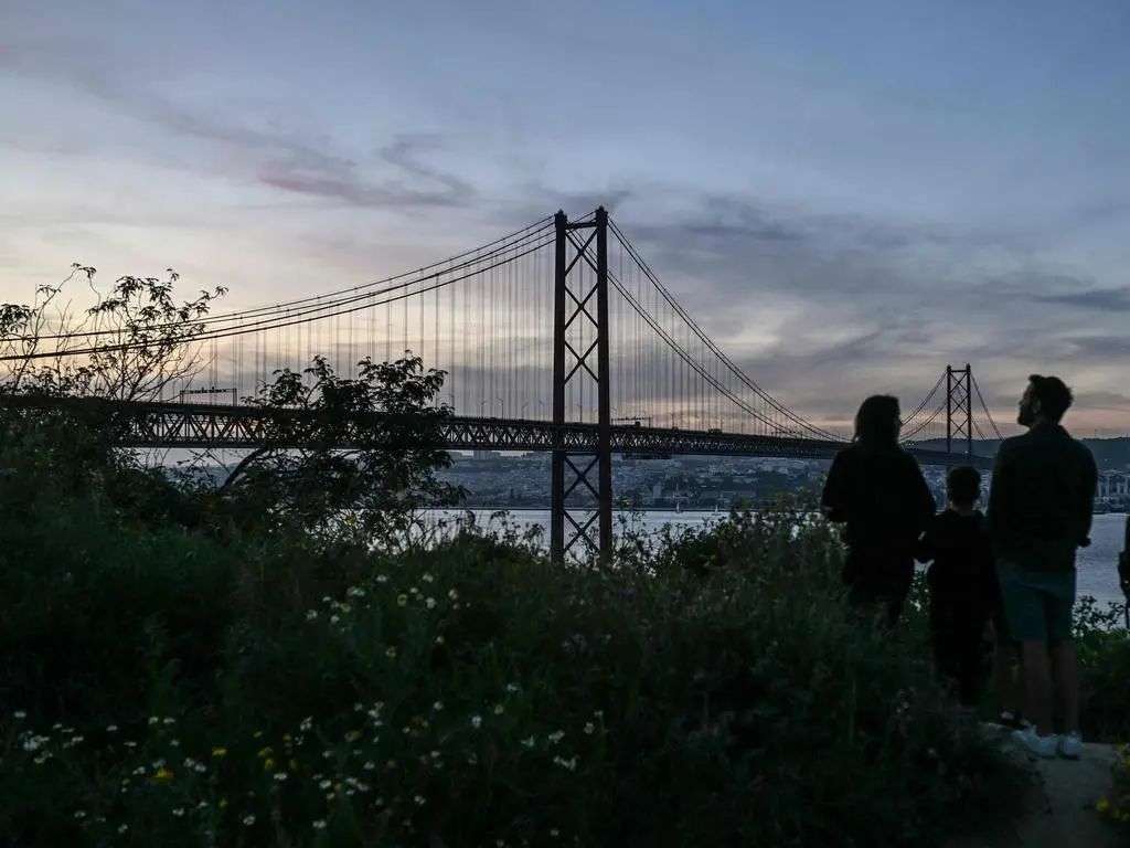 Normally lit up, the landmark 25 April bridge in Lisbon is in darkness. Picture: AFP