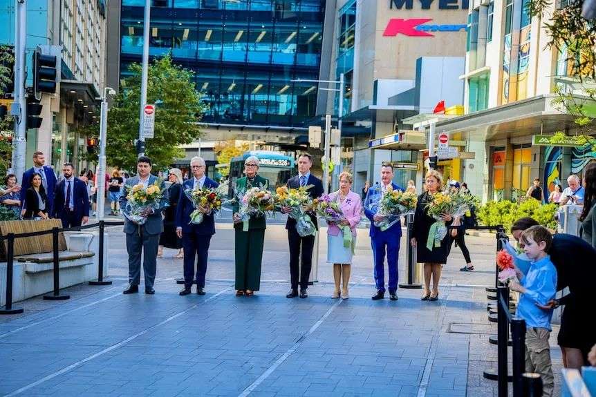 a number of dignitaries hold flowers about to lay them on the ground at the one year commemoration of bondi attack