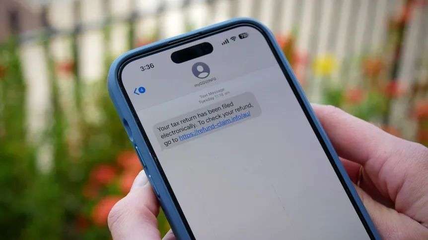 Hands hold a mobile phone displaying a scam text message.