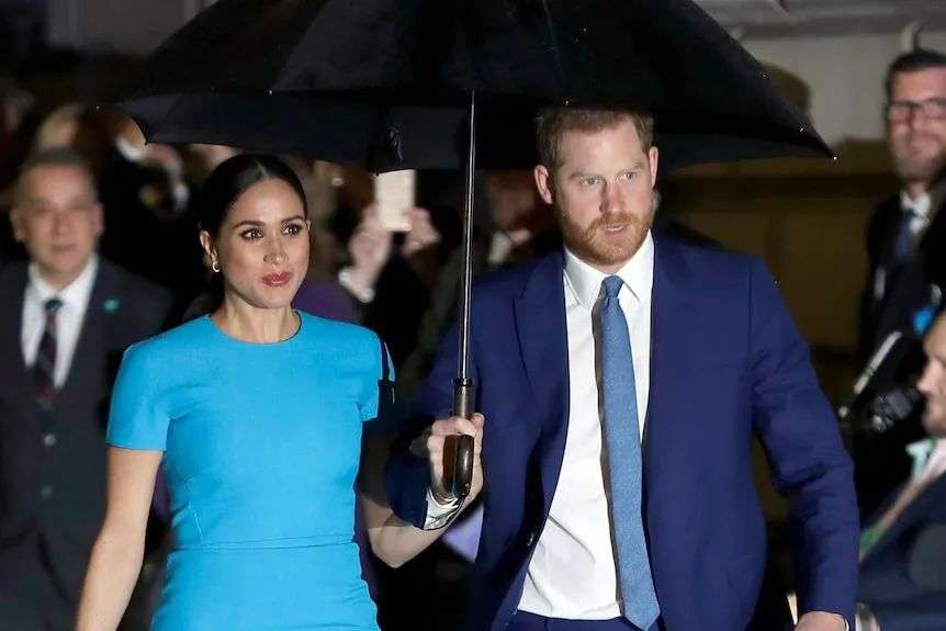 A woman and a man share an umbrella as they walk past a crowd of people