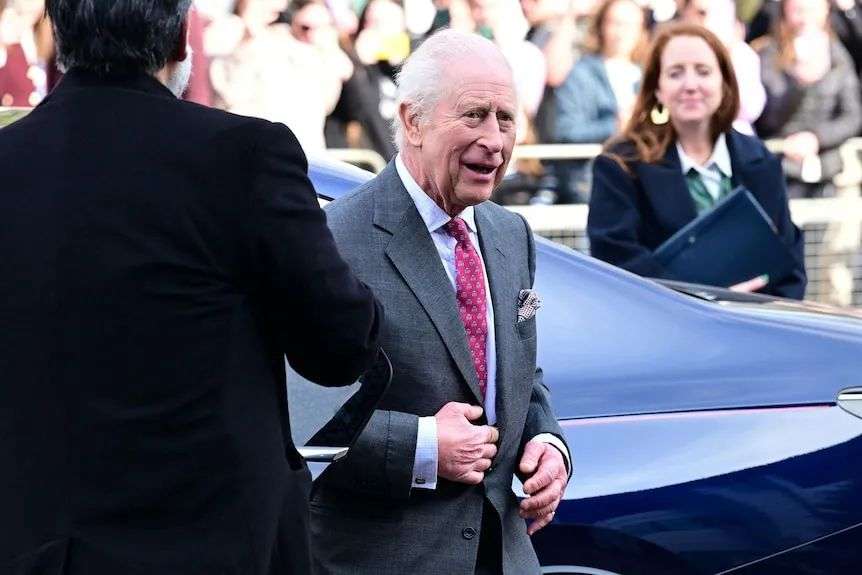 King Charles wearing a suit gets out of a car