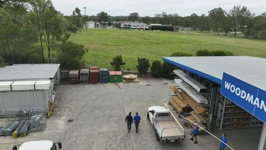 An aerial shot of a large open grass block. In the foreground is a hardware store where pallets and timber is lined up.