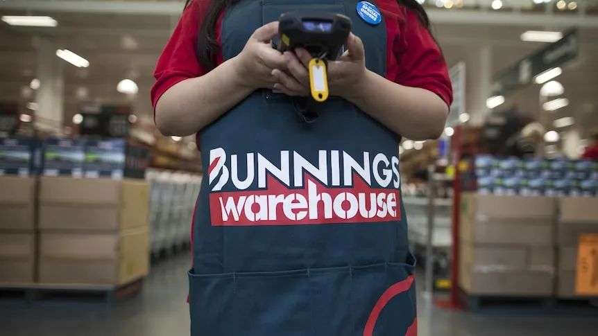 A person in a Bunnings apron stands in a Bunnings aisle.