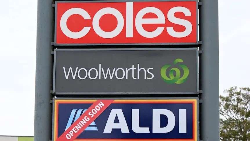 Signs for Coles, Woolworths and Aldi supermarkets outside a shopping centre.