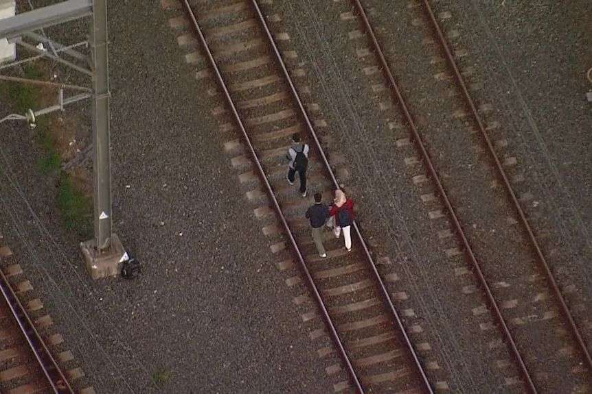 Passengers walk on train tracks after being stuck in train cables fell on