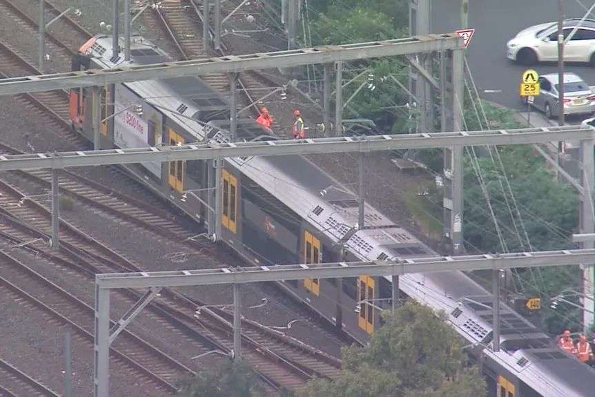 An aerial shot of a train halted on tracks with workers fixing the situation.