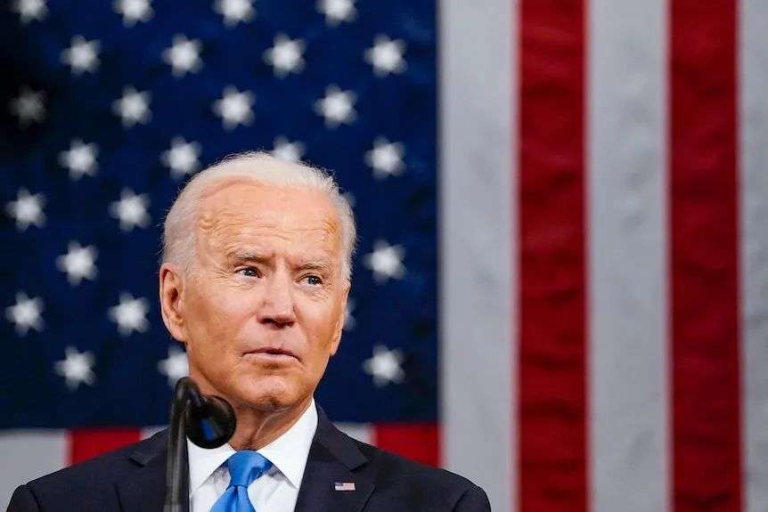 Joe Biden speaking into a microphone in front of an American flag
