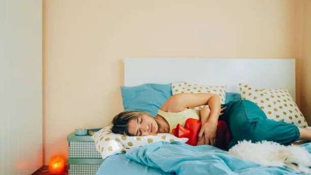 woman lying down clutching a hot water bottle to her abdomen
