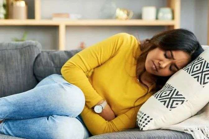 A woman in a yellow top and teens clutches her stomach on a couch