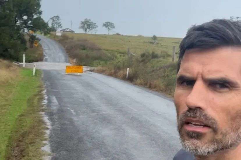 A man stands in front of a flooded section of road.