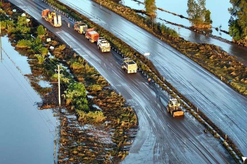 aerial shot of crews on the trucks clearing debris on a road after the floods