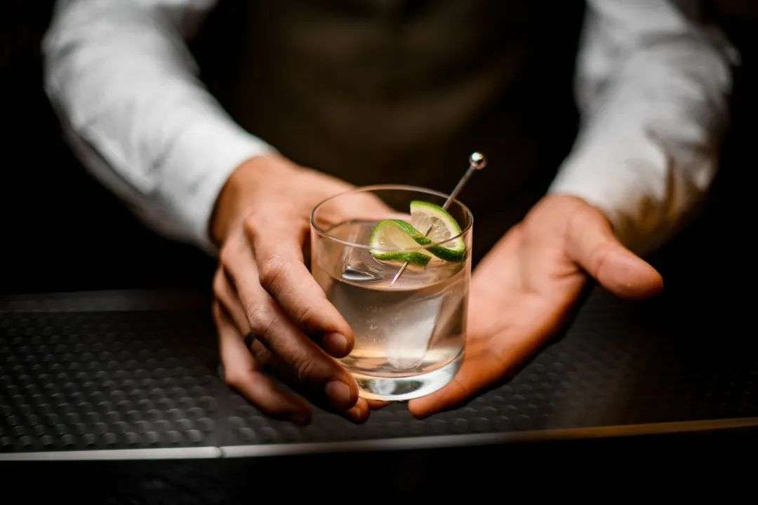 beautiful closeup on hands of man bartender holding glass with cold drink with ice cube decorated with lime