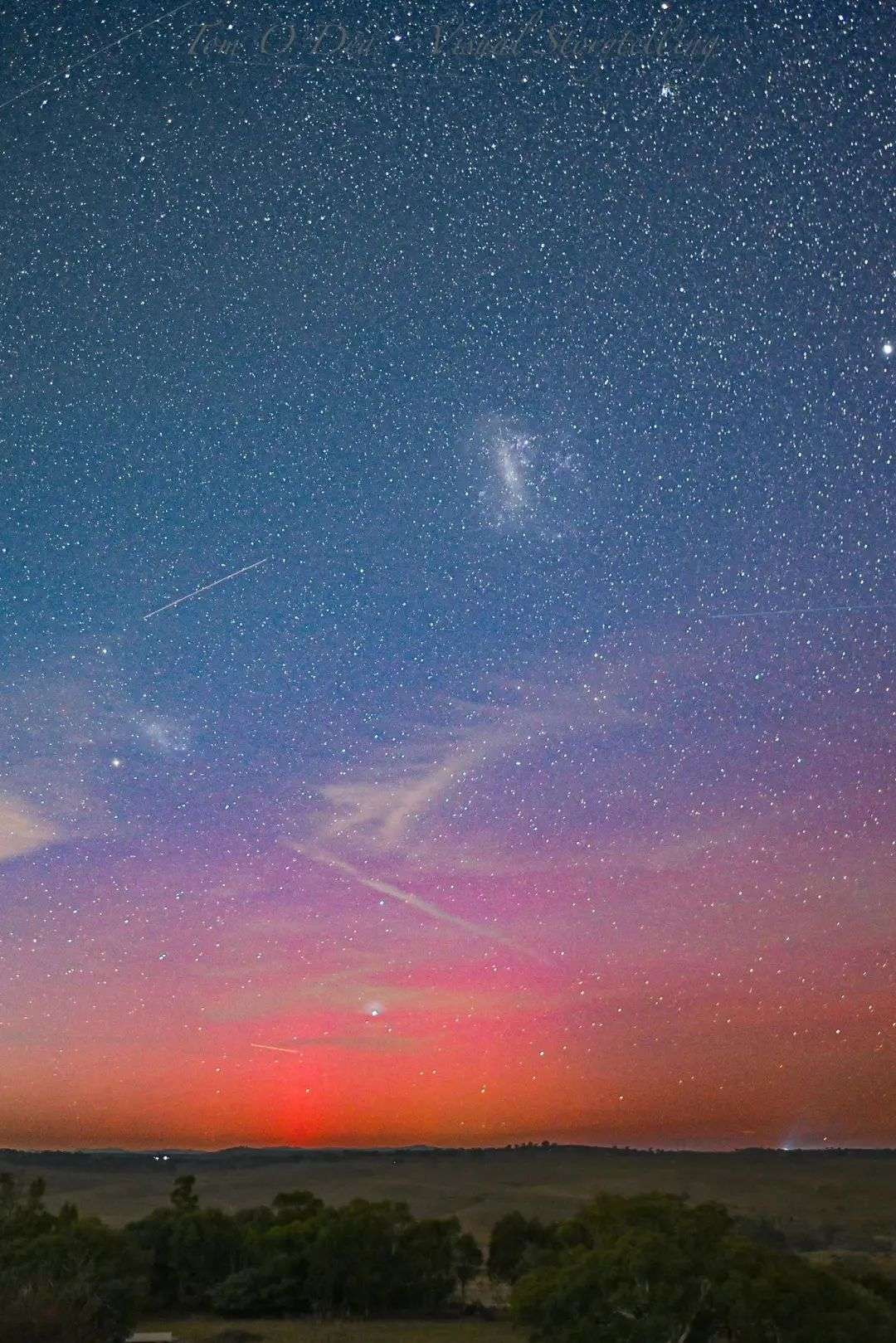 A pink and orange light is visible over the horizon in the night sky over Yass farmland