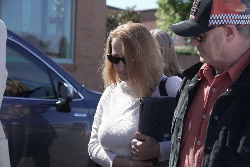 A blonde woman with sunglasses holds a binder