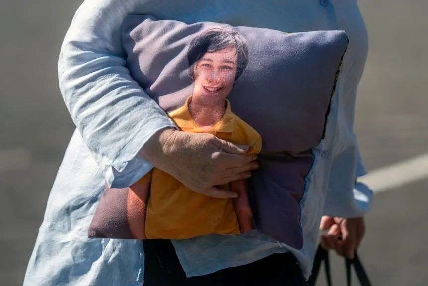 Closeup of a cushion featuring a picture of a smiling boy carried by a woman in a blue long-sleeved shirt.