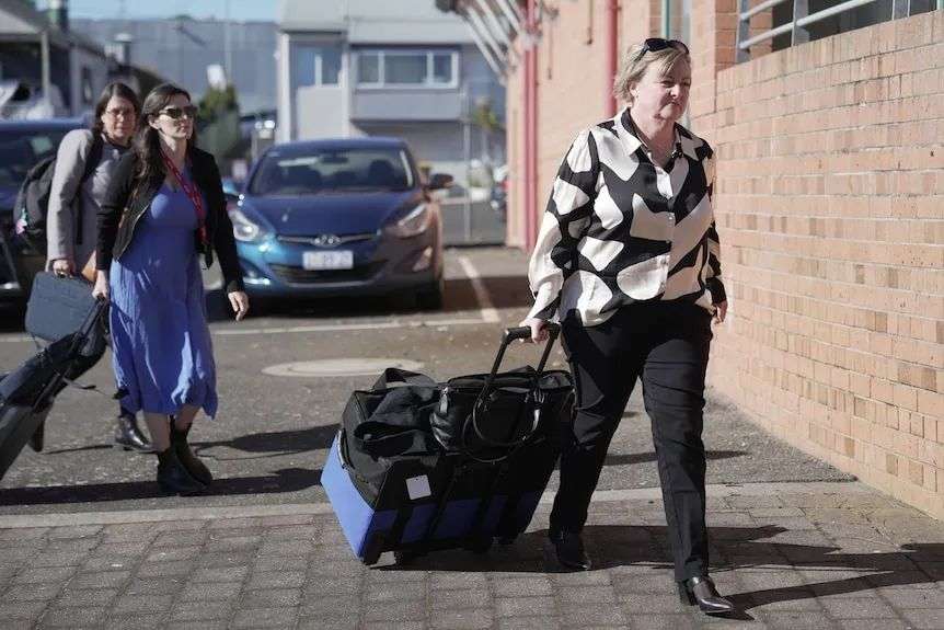 A woman pulls a bag on wheels outside a court house.