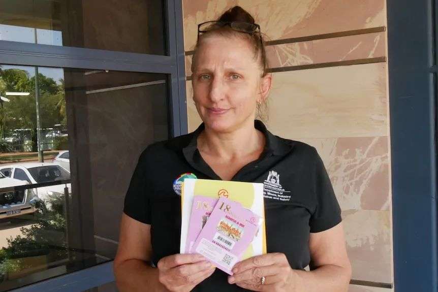 Woman in t-shirt holds up scratchie scam tickets and yellow envelope