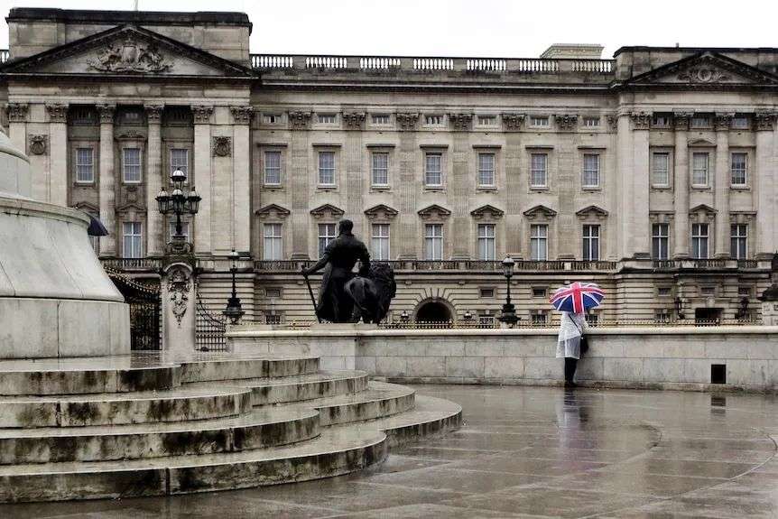 A lone tourist outside Buckingham Palace carrying a British flag umbrella