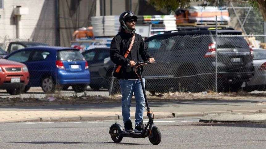 A man rides an e-scooter across an urban carpark.