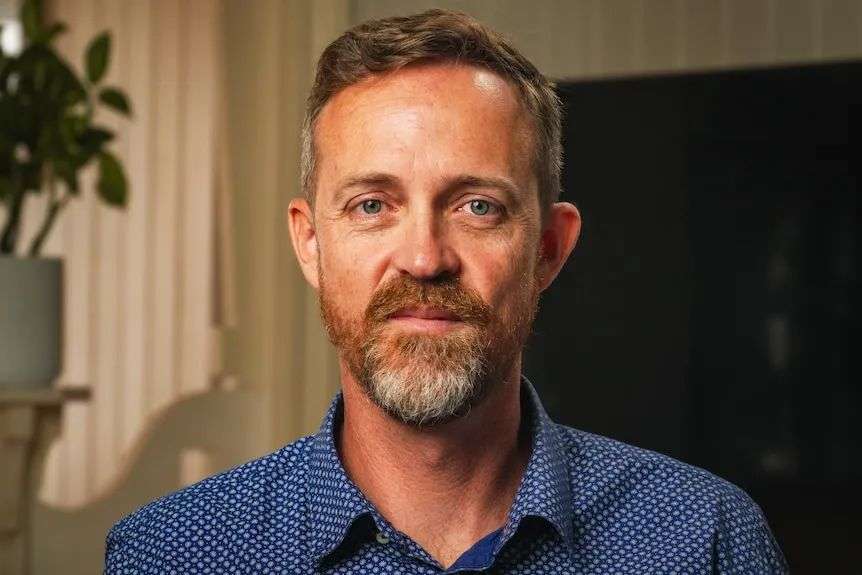 Man in a blue top with short hair and some facial hair.