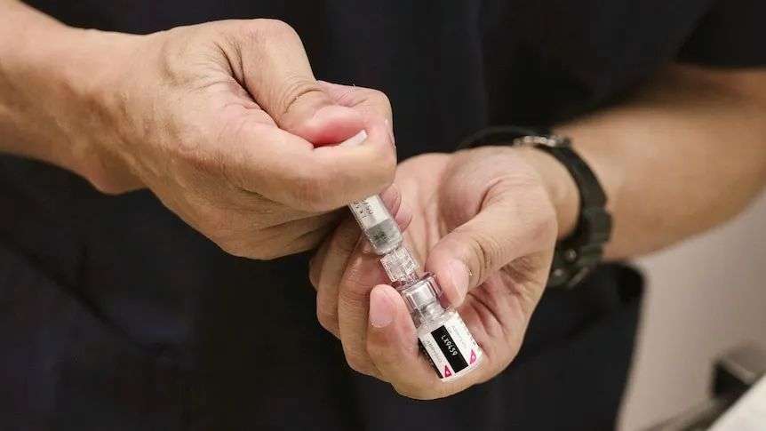 A close-up of hands filling a vaccination syringe with liquid from a vile.