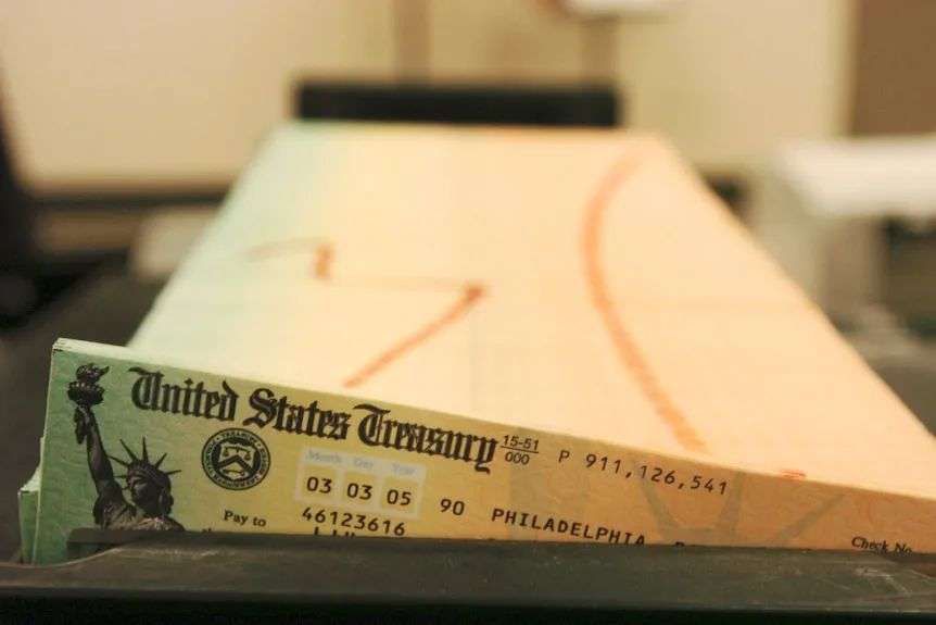 The corner of a US Treasury bank cheque poking up from a dark covering