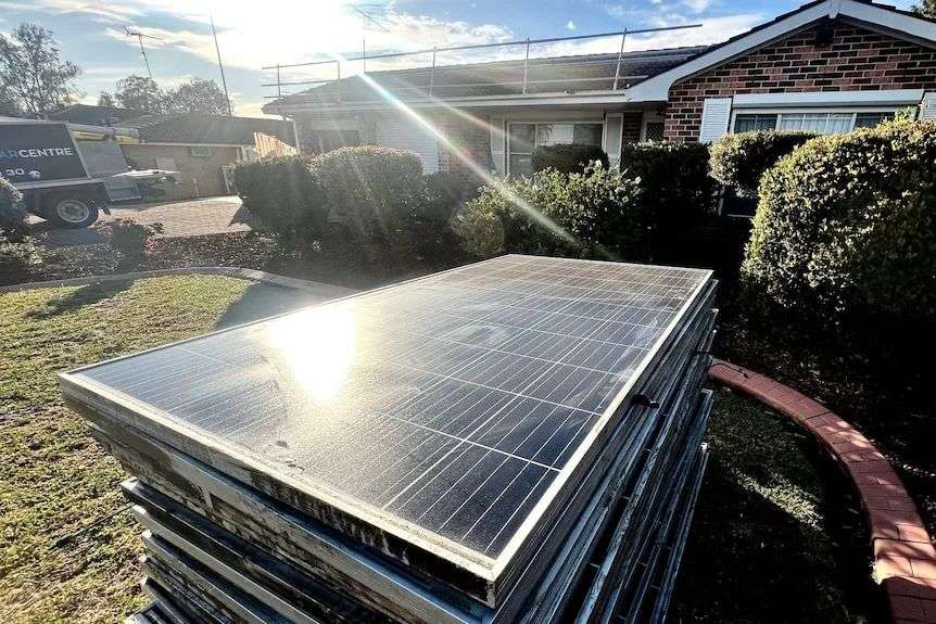 A pile of solar panels in front of a house reflect the sunlight