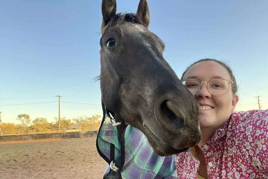 a female vet smiles as she rests her head next to a horse's head