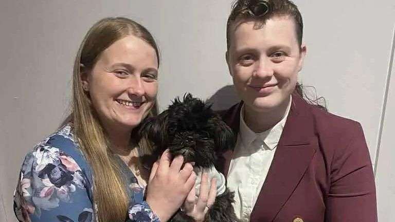 two women hold up a tiny black dog