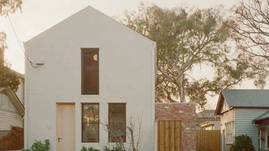 A small two story white brick house with pitched roof faces the street.