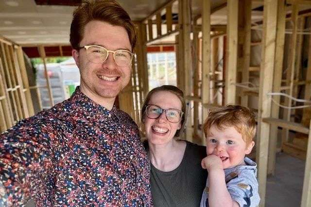 A young family stand next to wall frames inside the garage they are smiling at the camera