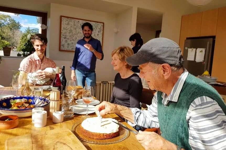 family sit around a table with birthday cake