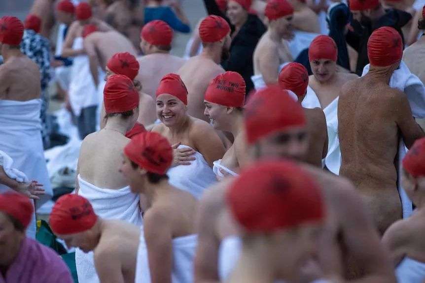 Post-dip exhilaration for nude swim participants in red caps.