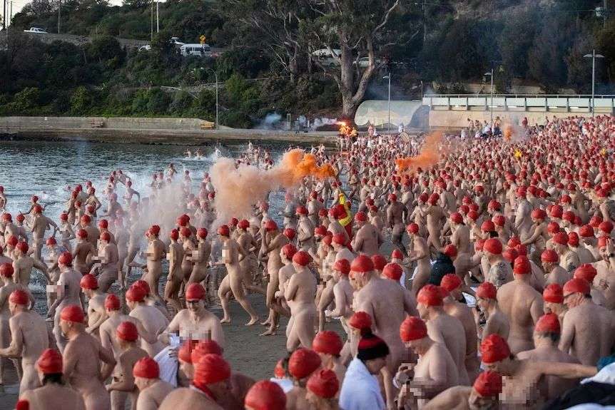 Hundreds of people in red caps but no other cloths run into the water.