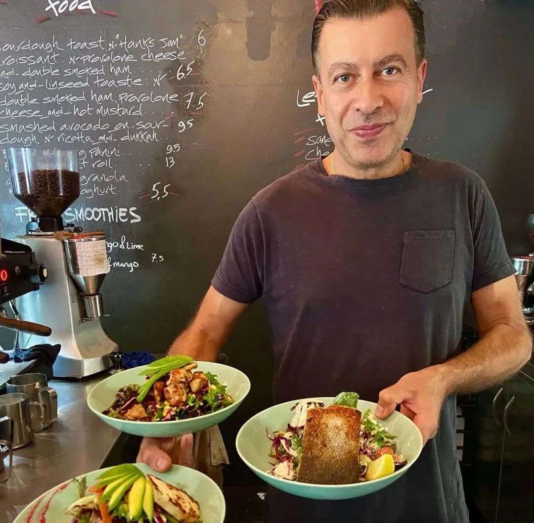 Franco Amitrano holds three plates and poses for a photo inside his cafe in Surry Hills, Cafe and Cuchina