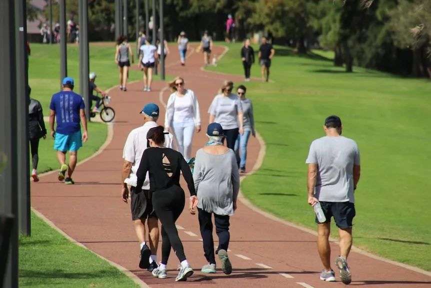 Dozens of people walking along a path next to green grass on a sunny day