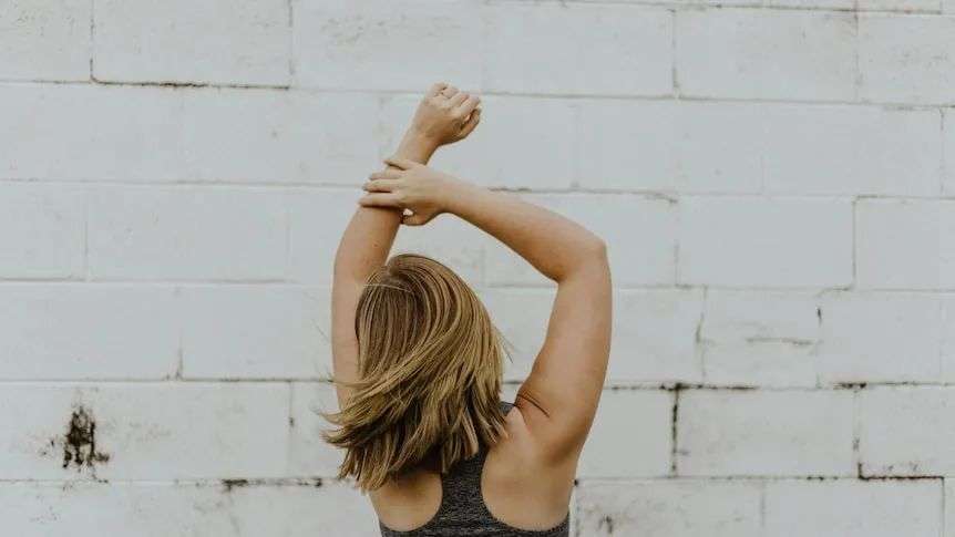 A photo of a woman wearing grey racerback top stretching, shot from behind
