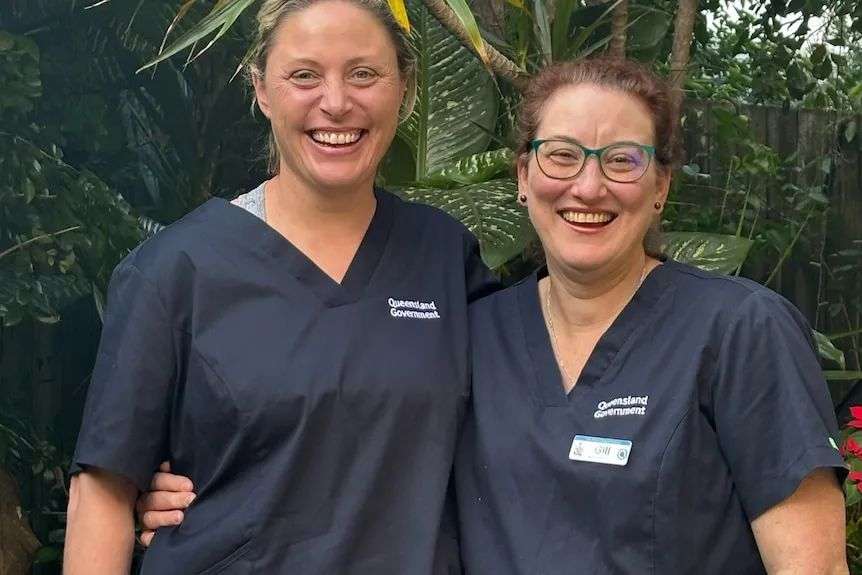 Two women stand together in Queensland Health uniforms.