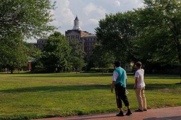 Two people walk on the Johns Hopkins campus, with its lush trees and red brick buildings.