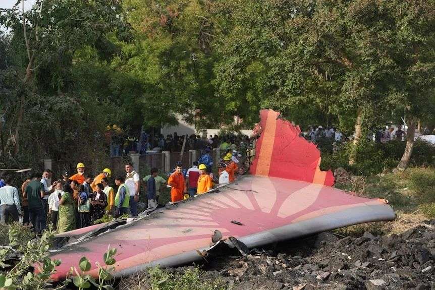 A piece of a broken plane sits surrounded by trees and emergency workers