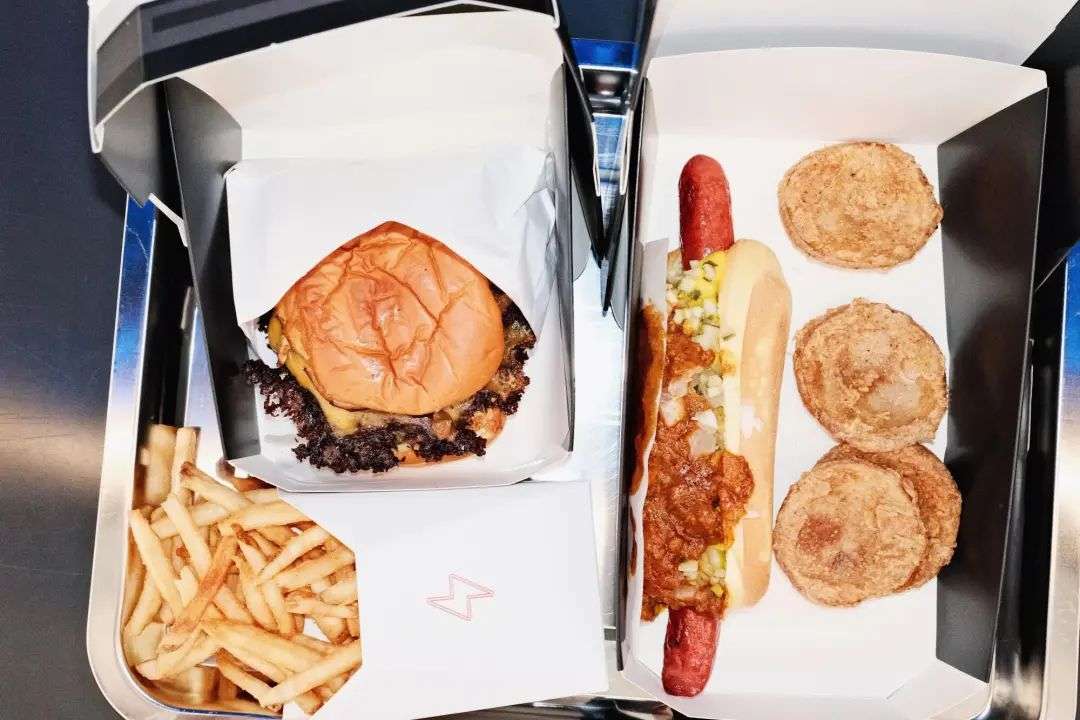 A Tesla smash burger, tallow fries, wagyu-chili hot dog and hash brown bites on a silver tray at the Tesla Diner in Hollywood