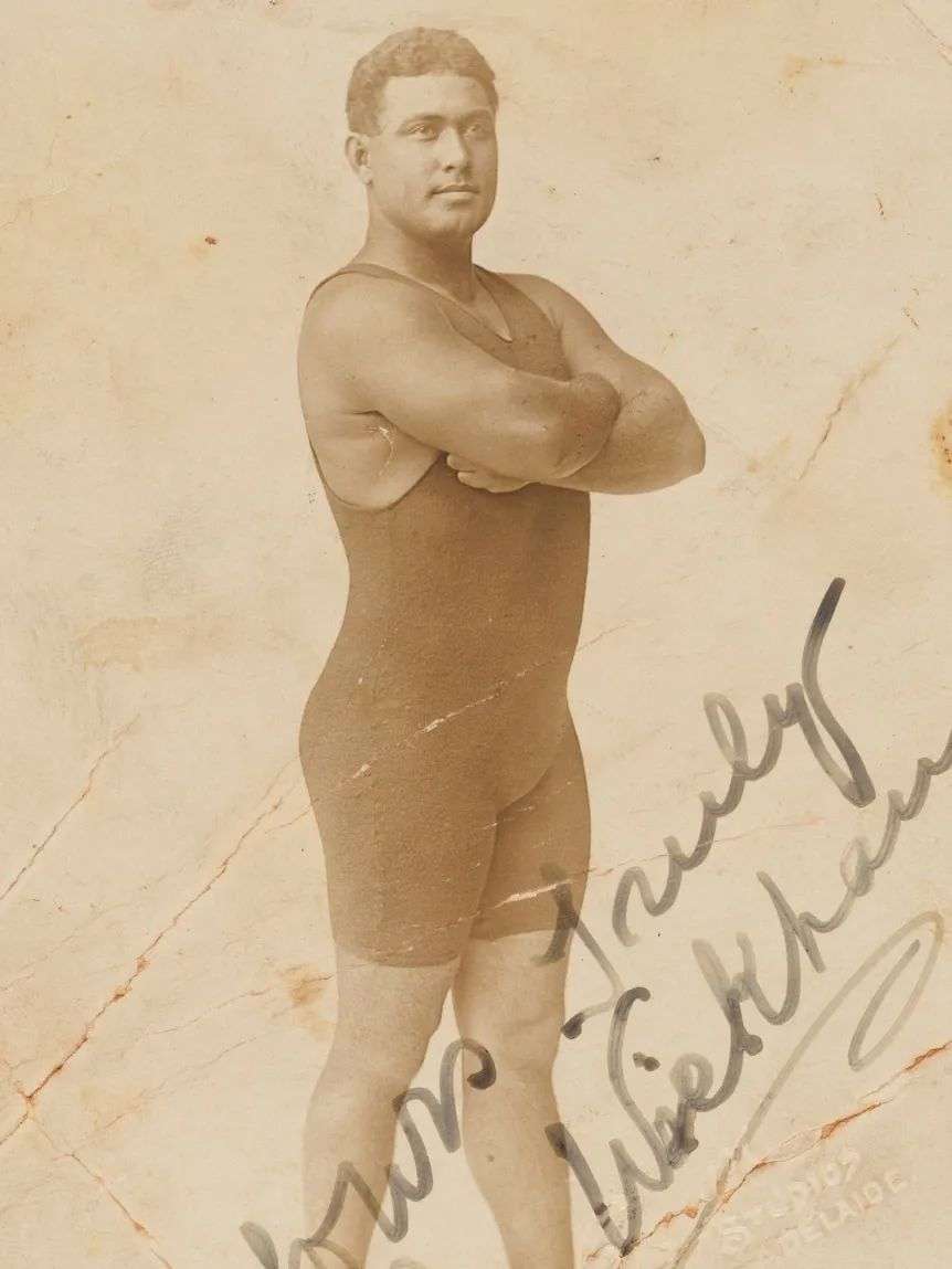 An early 1900s sepia photo of a man from the Solomon Islands in a swimsuit, with his arms crossed