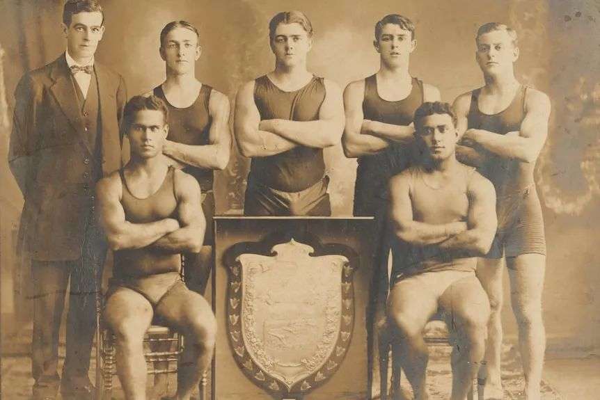 An early 1900s sepia photo of a men's swimming team, including two men from the Solomon Islands.