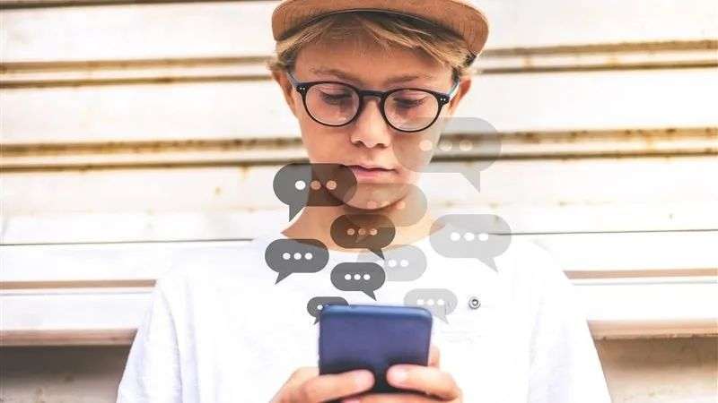 A young boy with a hat and glasses texting on a phone