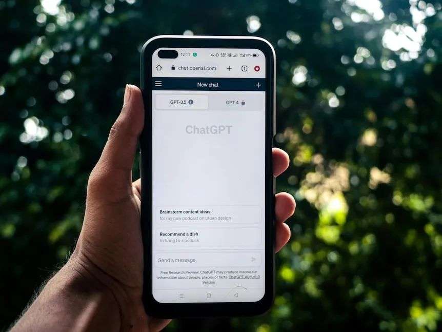 A hand holding up a phone displaying various uses of AI chatbot ChatGPT against a leafy backdrop