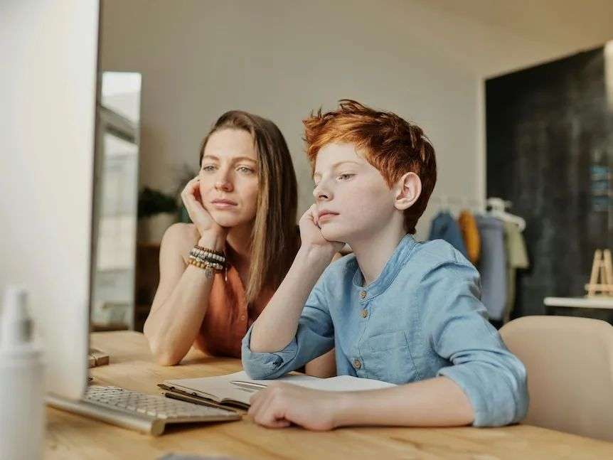 A parent seated next to child as they both face the computer