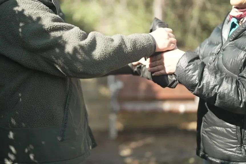 A person hands over a bag to another person in a park.